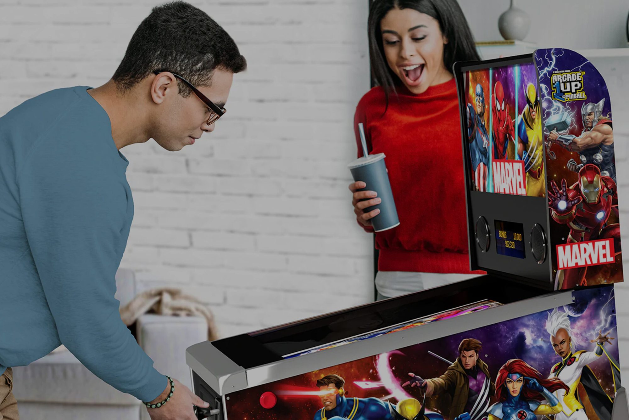 Marvel-Flipper mieten: zwei Personen spielen am Arcade1Up-Flipperautomaten vor einer Backsteinwand